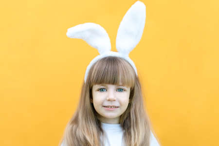 cheerful girl with rabbit ears on her head on a yellow background. Funny crazy happy child. Easter child. Preparation for the Easter holiday. promotional items. copy space for text, mockupの写真素材