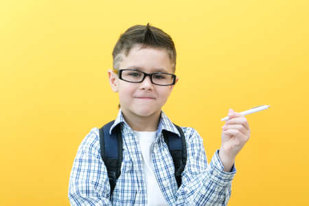 Photo of a smart schoolboy holding a pen in a white shirt on a yellow background. place for your text, copy spaceの写真素材