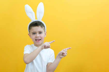 cheerful boy with rabbit ears on his head on a yellow background. Funny happy child points his...
