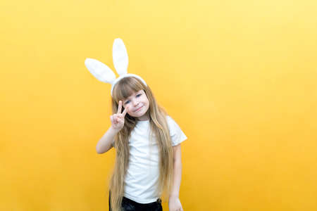 cheerful girl with rabbit ears on her head on a yellow background. Funny crazy happy child. hands like a rabbit. Preparation for the Easter holiday. copy space for text, mockupの写真素材