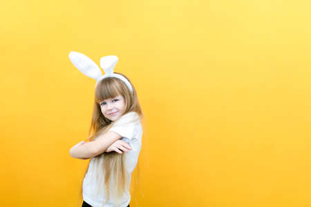 cheerful girl with rabbit ears on her head on a yellow background. Funny crazy happy child. Easter child. Preparation for the Easter holiday. promotional items. copy space for text, mockupの写真素材