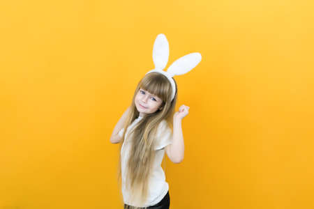 cheerful girl with rabbit ears on her head on a yellow background. Funny crazy happy child. Easter child. Preparation for the Easter holiday. promotional items. copy space for text, mockupの写真素材