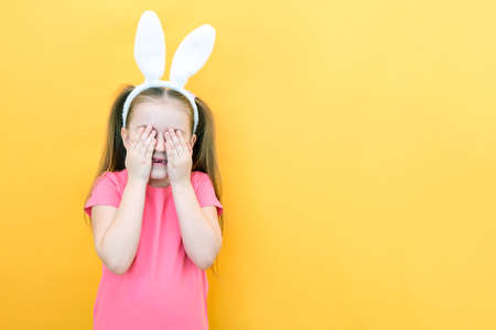 cheerful girl with rabbit ears on her head on a yellow background. Funny crazy happy child. Easter...