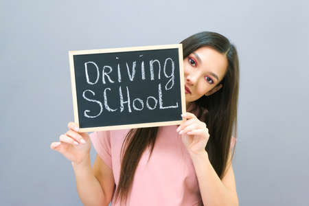 Driving school idea and concept, student driver passed the exam, drivers license, beautiful happy young woman, holding a car in her hand. on a gray background. plate with the inscription Driving schoolの写真素材