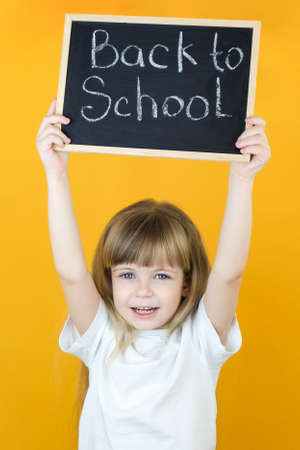 schoolgirl holding a tablet in her hands with the inscription Back to school on a yellow background. happy school girlの写真素材