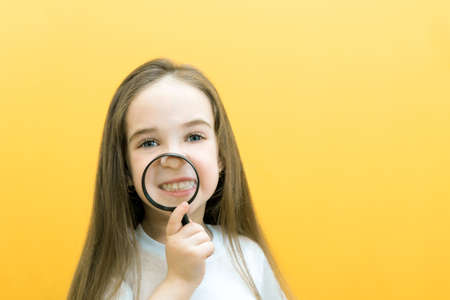 Funny girl showing teeth through a magnifying glass, isolated on yellow background. Positive human...
