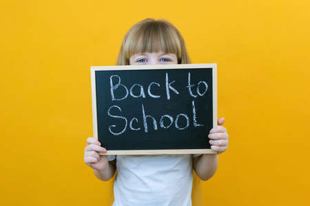 schoolgirl holding a tablet in her hands with the inscription Back to school on a yellow background....