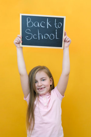 schoolgirl holding a tablet in her hands with the inscription Back to school on a yellow background. happy school girlの写真素材