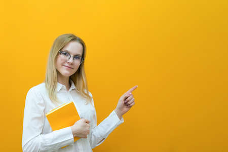 Young beautiful blonde student girl in glasses holds books on an isolated yellow background.の写真素材