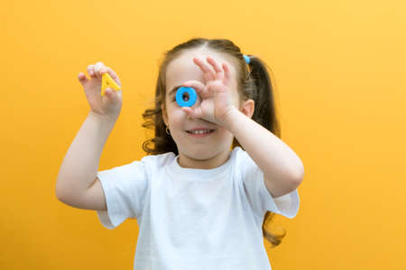speech therapy. Toddler girl holding the letter O and A in her hands. Classes with a speech therapist. girl on isolated yellow backgroundの写真素材