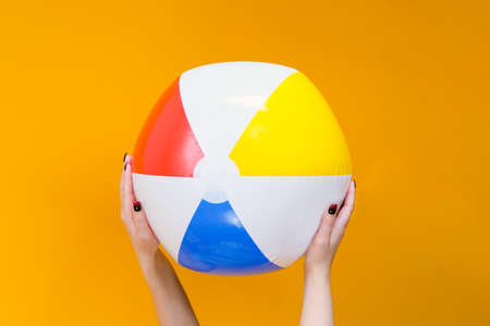 inflatable ball for playing in the water and on the beach in hands on a yellow background. vacation concept, sea, beach, swimming poolの写真素材
