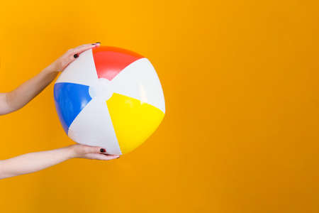 inflatable ball for playing in the water and on the beach in hands on a yellow background. vacation concept, sea, beach, swimming poolの写真素材