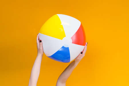 inflatable ball for playing in the water and on the beach in hands on a yellow background. vacation concept, sea, beach, swimming poolの写真素材