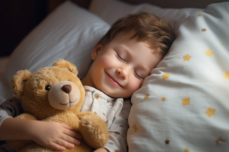 boy sleeps sweetly in bed with a toy bear in his arms under the blanketの素材