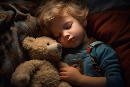 boy sleeps sweetly in bed with a toy bear in his arms under the blanketの素材