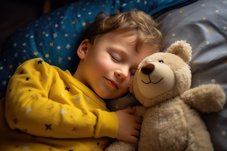 boy sleeps sweetly in bed with a toy bear in his arms under the blanketの素材