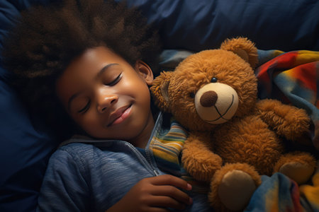 a darkskinned boy sleeps sweetly in bed with a toy bear in his arms under the blanketの素材