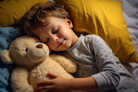 boy sleeps sweetly in bed with a toy bear in his arms under the blanketの素材