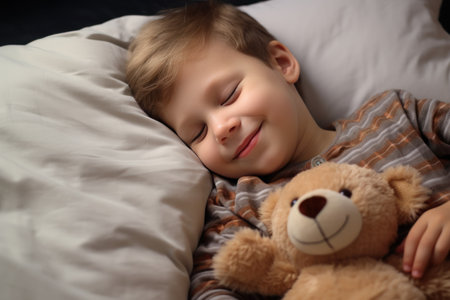 boy sleeps sweetly in bed with a toy bear in his arms under the blanketの素材