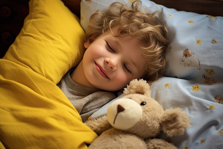 boy sleeps sweetly in bed with a toy bear in his arms under the blanketの素材