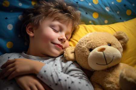 boy sleeps sweetly in bed with a toy bear in his arms under the blanketの素材