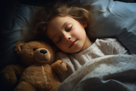 girl sleeps sweetly in bed with a toy bear in his arms under the blanketの素材