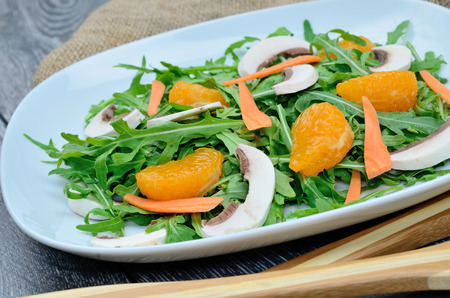 salad arugula with mushroom and mandarin in white dish on gray wooden tableの写真素材