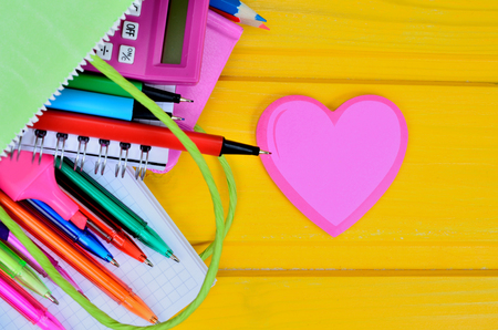 supplies for school in bag and paper heart on yellow wooden tableの写真素材
