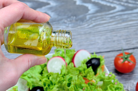 hand hold bottle of olive and salan on gray wooden tableの写真素材