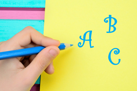 child hand hold pencil and letter a b c on yellow paper