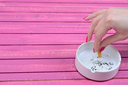 hand of woman crush a cigarette in ashtray on pink wooden table