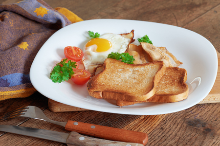 Breakfast with scrambled eggs, bacon, toast and fresh vegetables.の写真素材