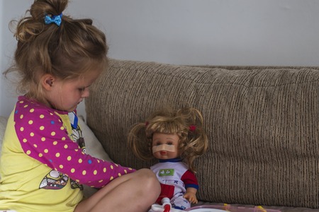 Girl playing a doctor with her doll at homeの写真素材