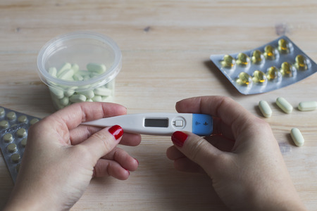 Thermometer in hands on the background of medical pills