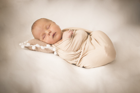 Newborn baby in a winding on a beige backgroundの写真素材