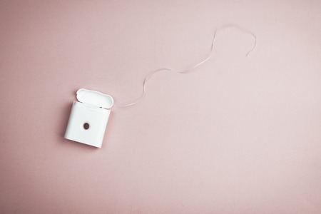 Dental floss in a white plastic container on a pink background