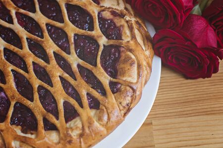 Cherry pie and a bouquet of roses next to it on a tableの写真素材