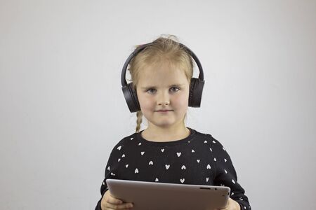 Beautiful girl with headphones and with a tablet looks into the camera