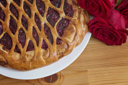 Close-up on a piece of cherry pie and a bouquet of red roses on a tableの写真素材