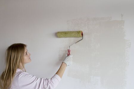 Woman enthusiastically and painstakingly paints a wall in whiteの写真素材