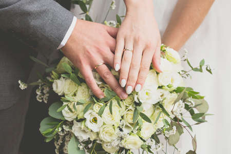Hands of the bride and groom on a bouquet of flowers