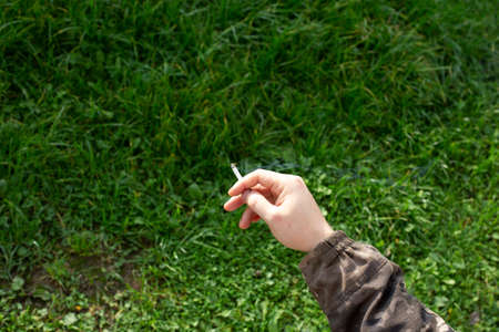 Cigarette in a mans hand on a background of summer grass.の写真素材