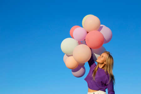 A young Caucasian girl launches a bunch of colorful balloons into the sky. Girl on a background of blue sky smiles and hold balloons.の写真素材
