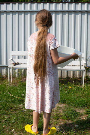 The girl stands with her back and holds a plastic basin in her hands. The child helps with household chores.の写真素材