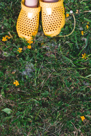 Childrens feet in yellow rubber slippers stand on the grass.