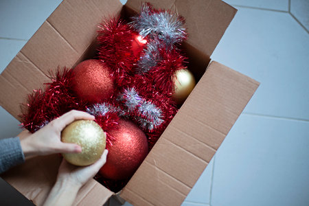 Womens hands take New Years balls for the Christmas tree from a box standing on the floor. Red and...