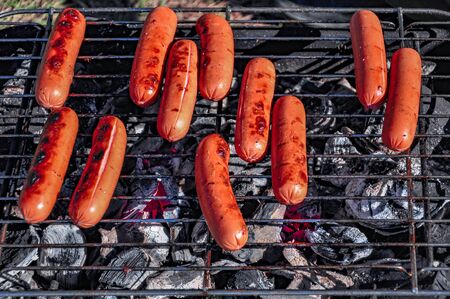 Standing on the grass, a small portable picnic grill with burning coals and sausages roasting on the grill, brightly lit by the rays of the setting sunの写真素材