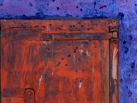 An old rusty iron gate with bullet holes and a large padlock