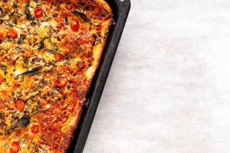Fresh delicious hot pizza with mushrooms, cherry tomatoes, Basil and Parmesan on a rectangular pan on a light background with copy space. Homemade pizza bakingの写真素材
