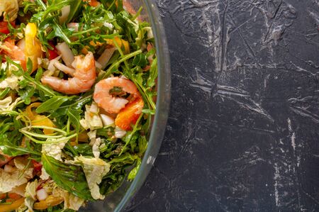 Fresh salad of king prawns, sweet bell peppers, cherry tomatoes, Chinese cabbage, tangerines, arugula and olive oil in a glass bowl on a dark backgroundの写真素材